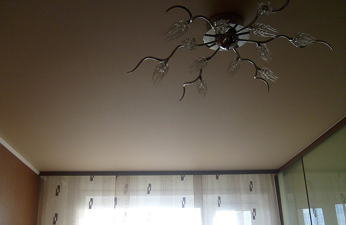 Кремовый матовый натяжной потолок с люстрой в спальне