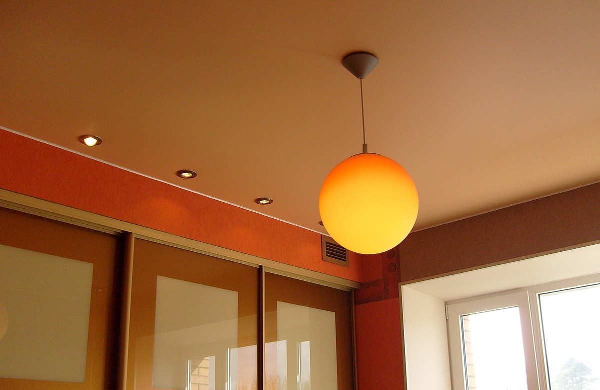 Оранжевый матовый натяжной потолок со светильниками и люстрой