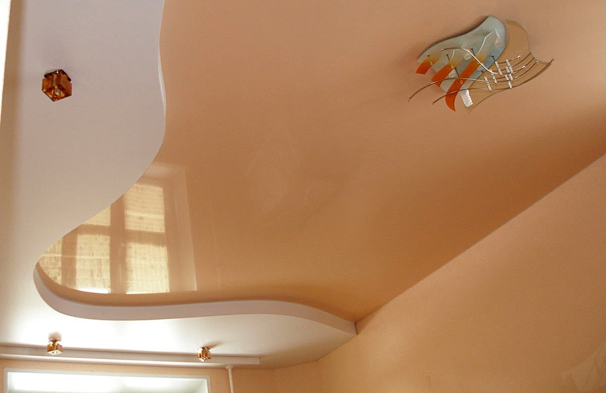 Персиковый глянцевый натяжной потолок с люстрой в коробе из гипсокартона